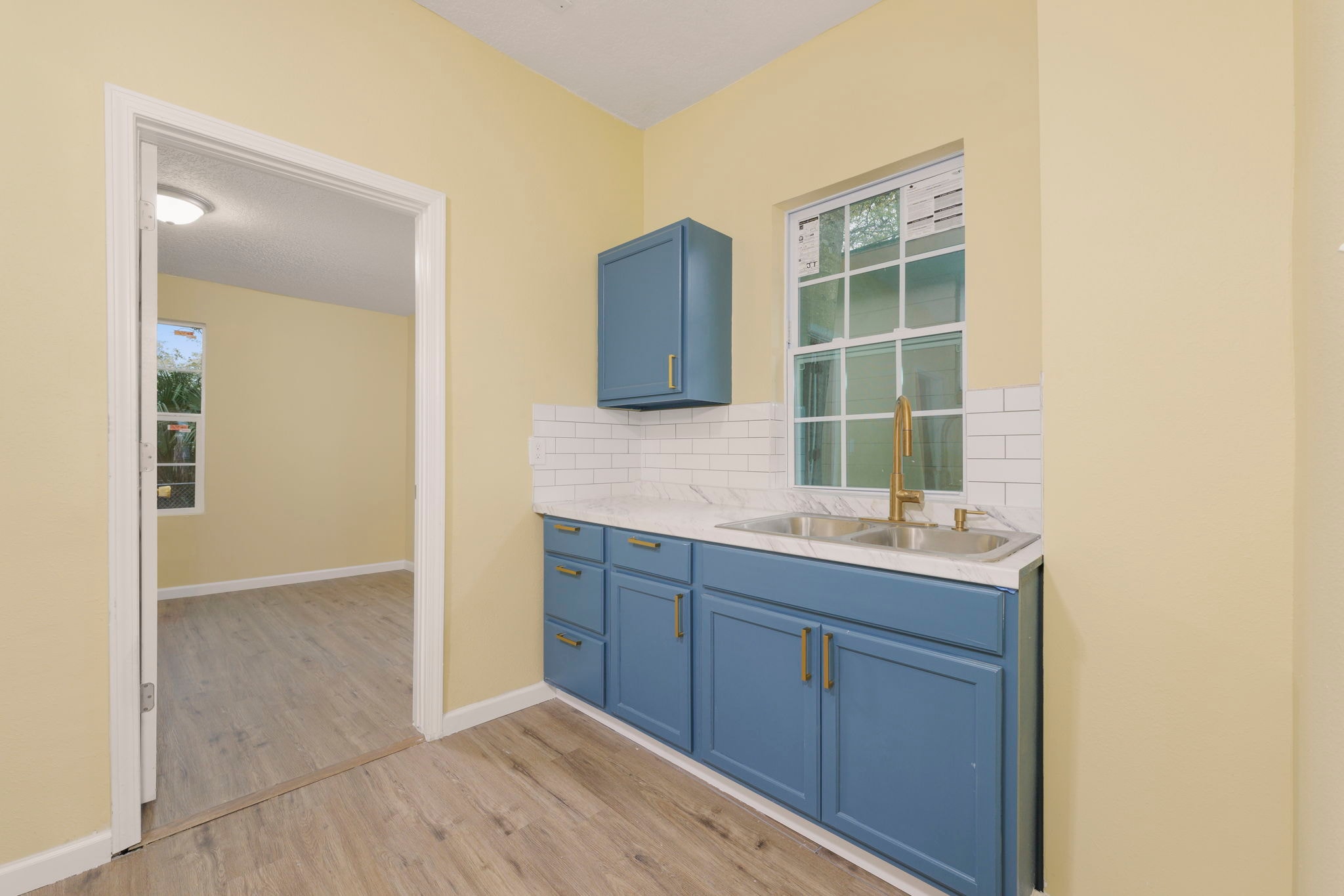 Kitchen sink area – blue cabinets, gold faucet, marble countertop and subway tile