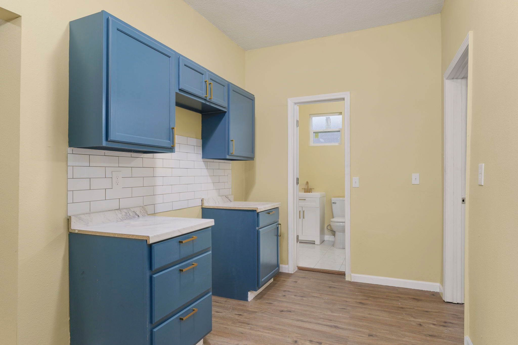 Kitchen with blue cabinets, subway tile, marble counters and bathroom visible through doorway