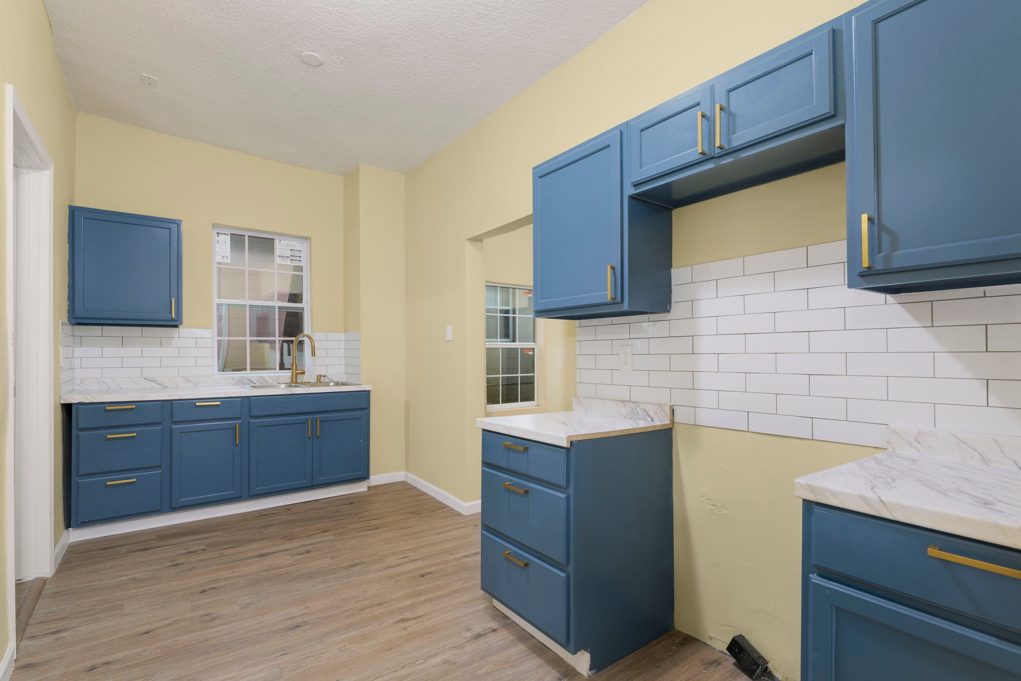 Full kitchen view – blue cabinets, marble countertops, subway tile backsplash, two windows