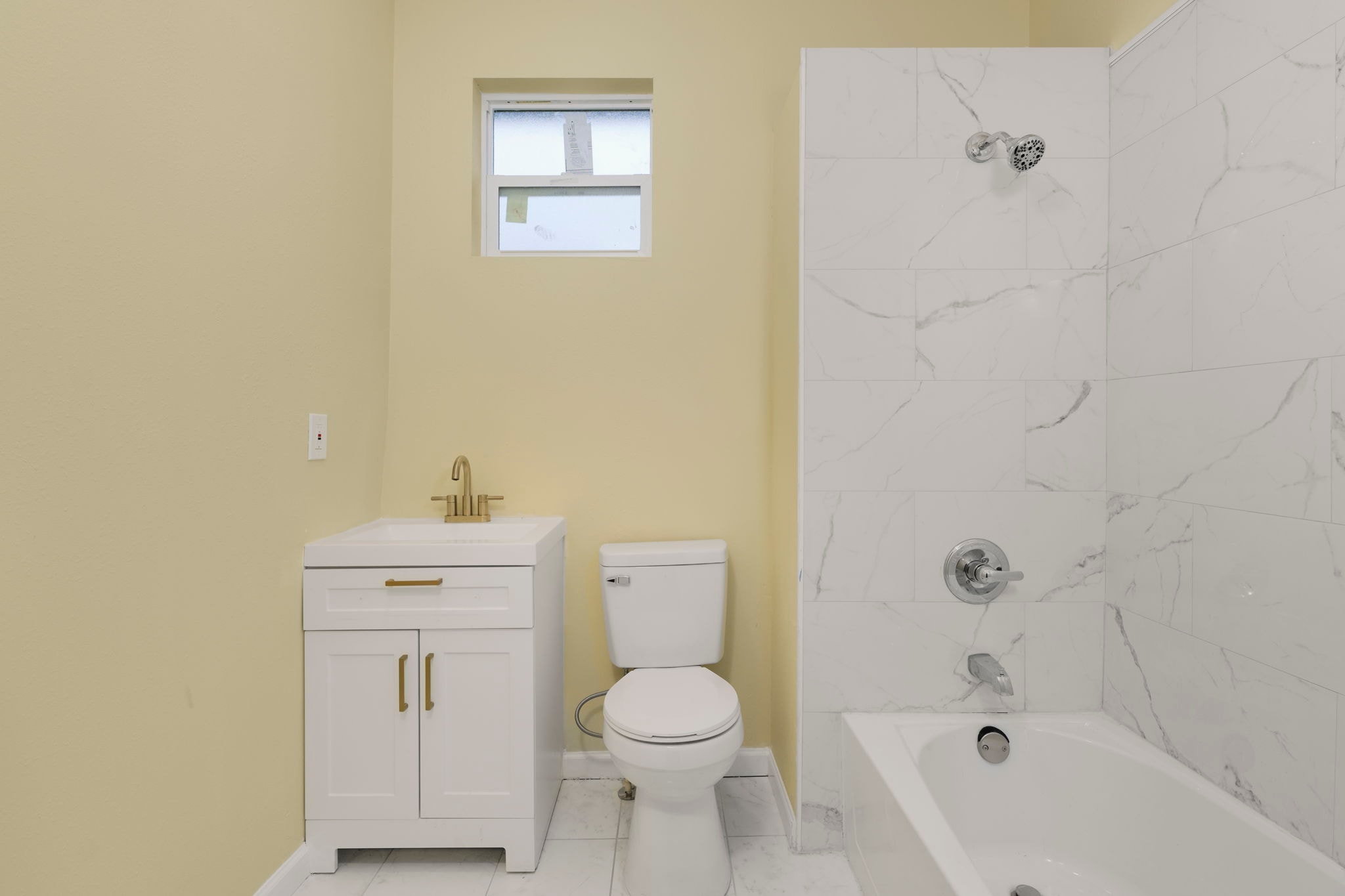 Renovated bathroom with white vanity, gold fixtures, marble tile tub surround