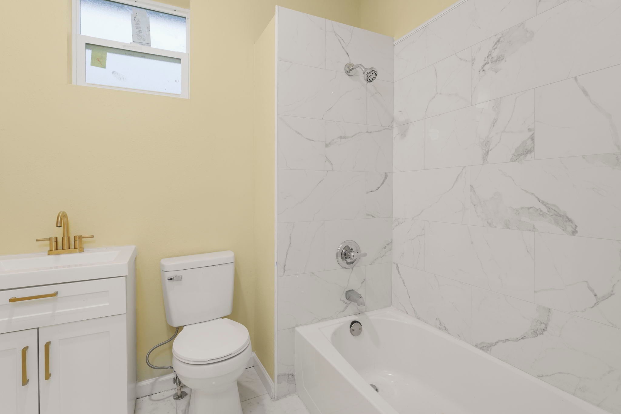 Bathroom with marble tile shower and tub, white vanity and gold hardware