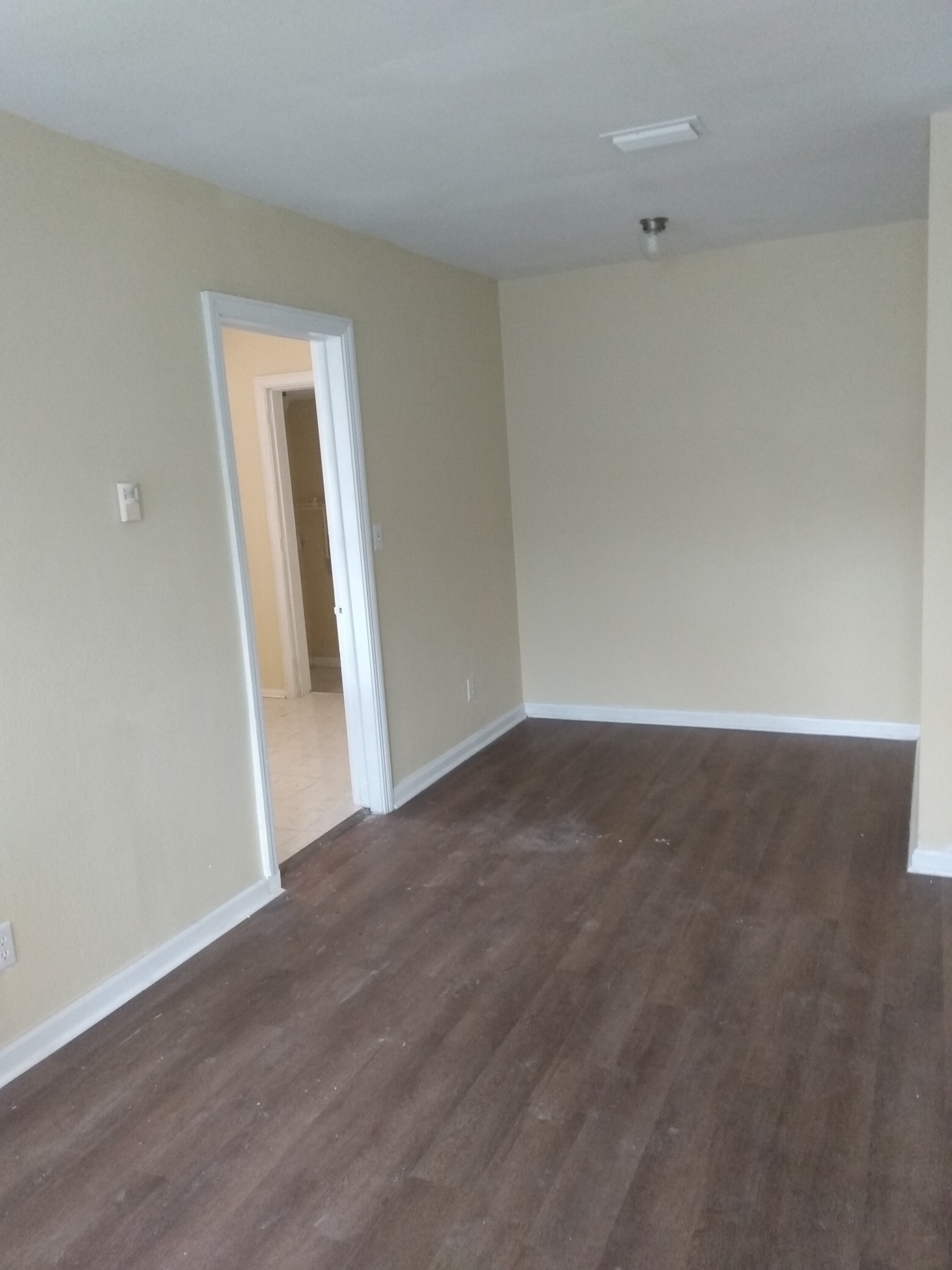 Open living area – cream walls, dark wood floors, doorway to tiled room