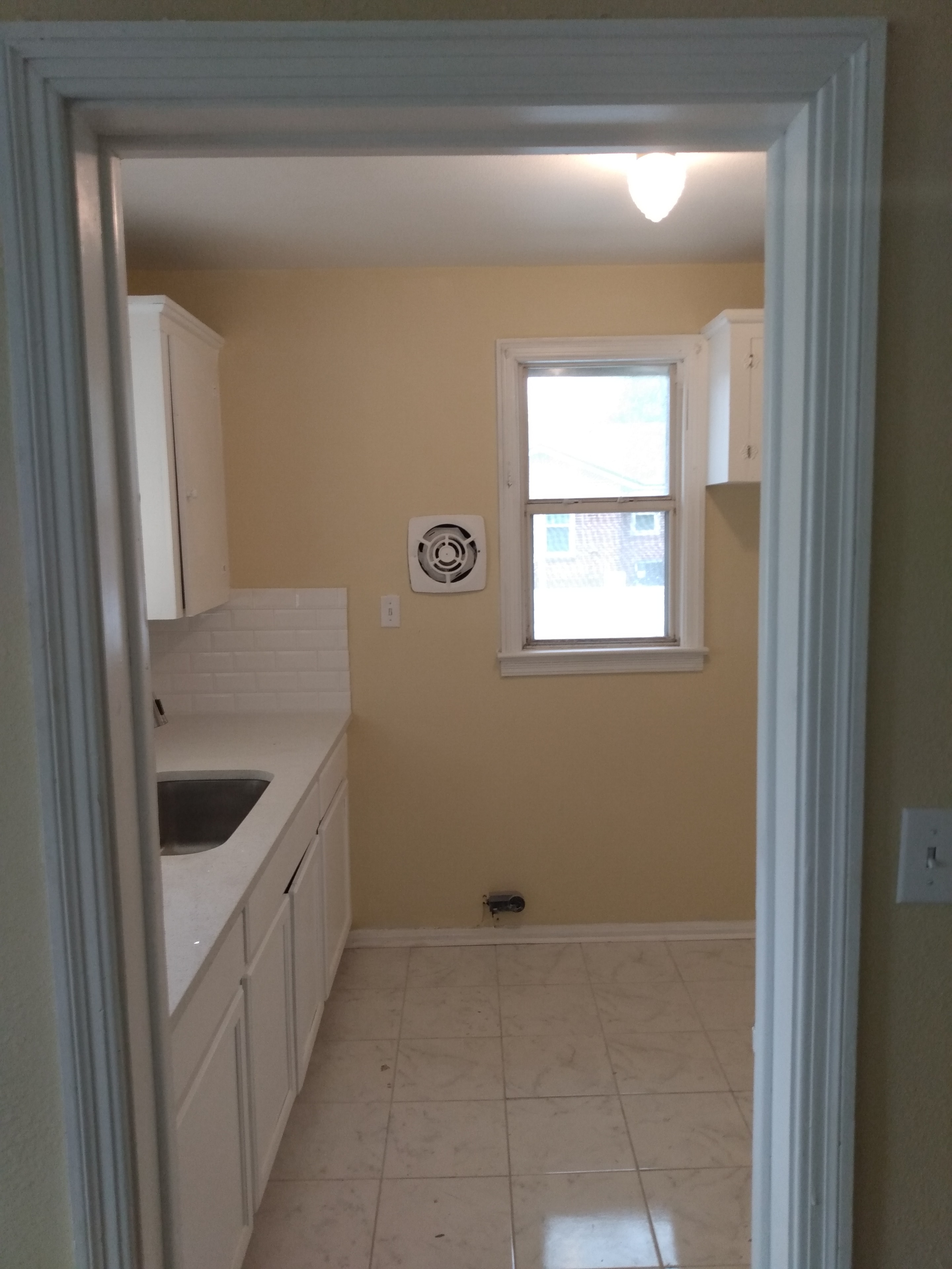 Kitchen doorway view – white cabinets, subway tile backsplash, tile floor, window