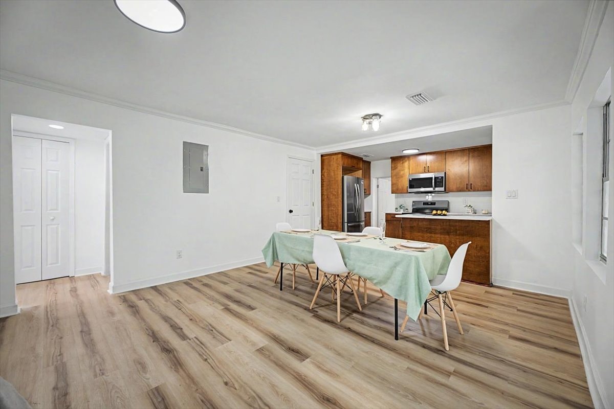 Open dining and kitchen – white walls, crown molding, LVP floors, dining table set, kitchen visible in background