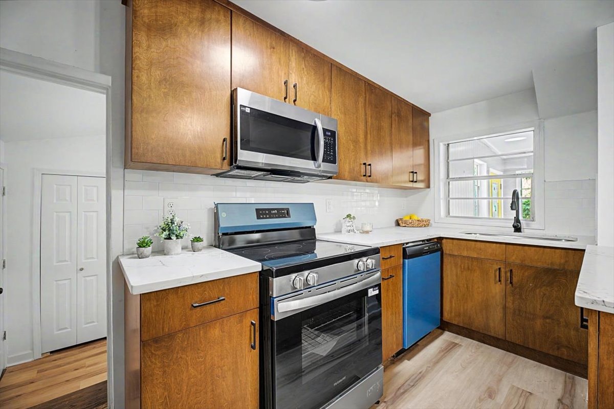 Kitchen range wall – walnut upper and lower cabinets, subway tile, stainless range, microwave and blue mini fridge