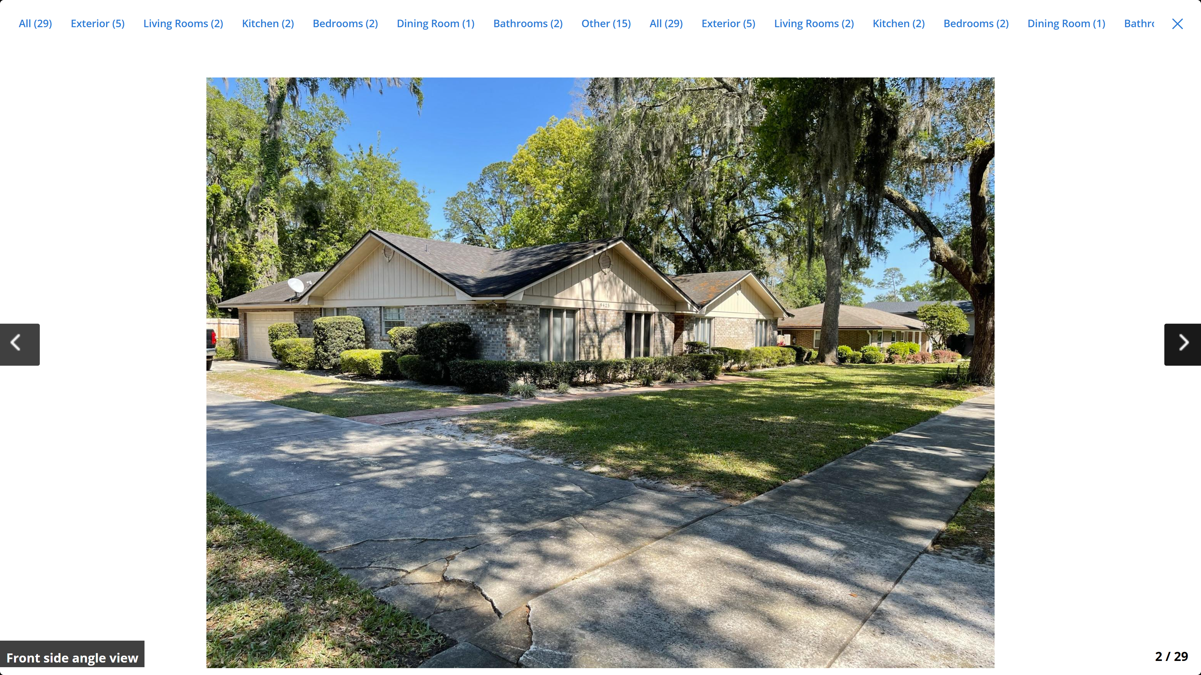 Front side angle view – brick ranch home with mature oak trees and manicured hedges